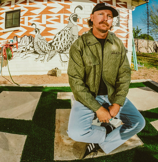 Man in a green rain camo jacket sitting in front of a wall mural